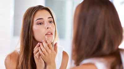 Chica quitandose un grano en el espejo